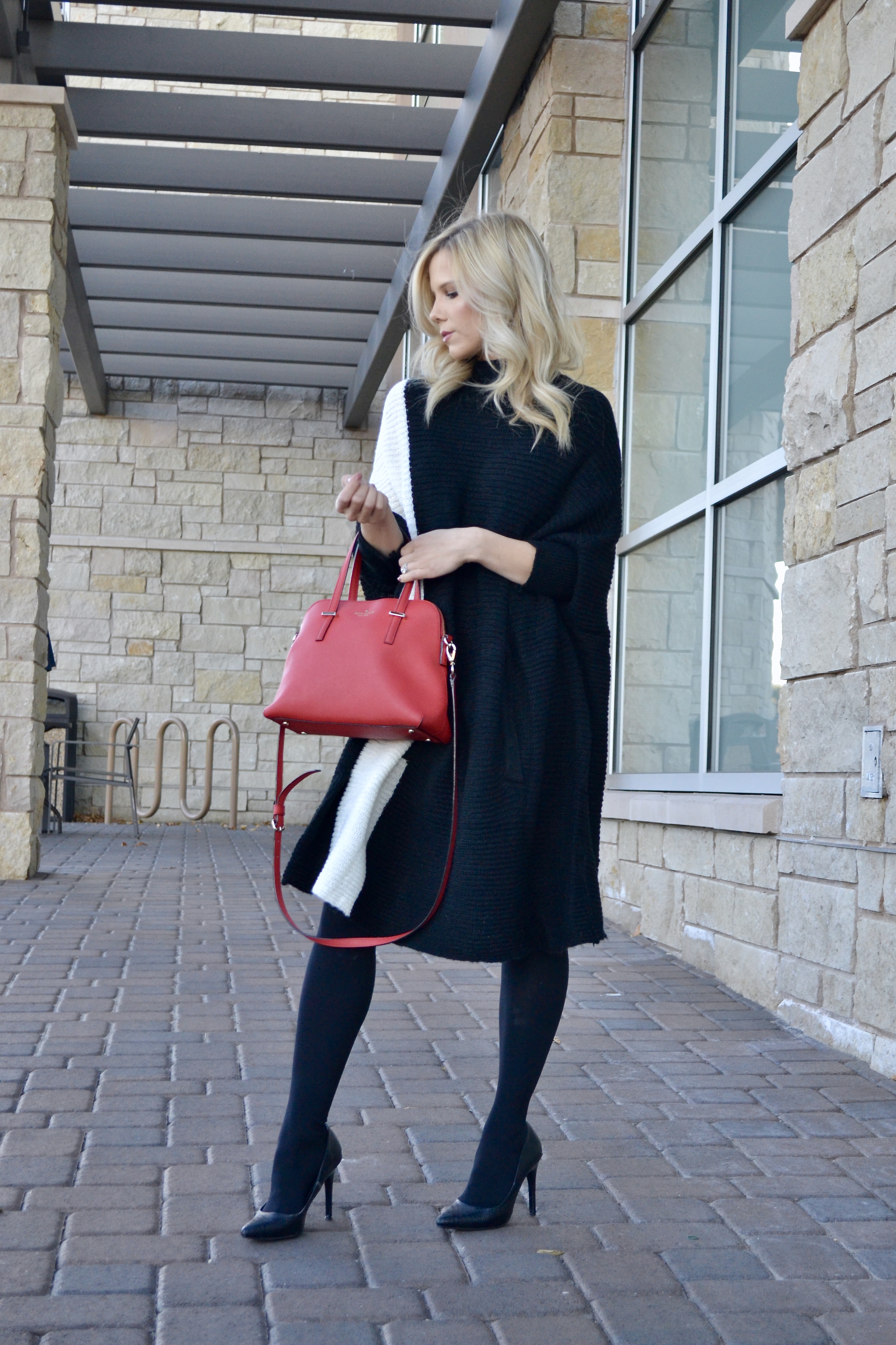 black and white color block sweater with black tights, heels, and a red Kate Spade purse